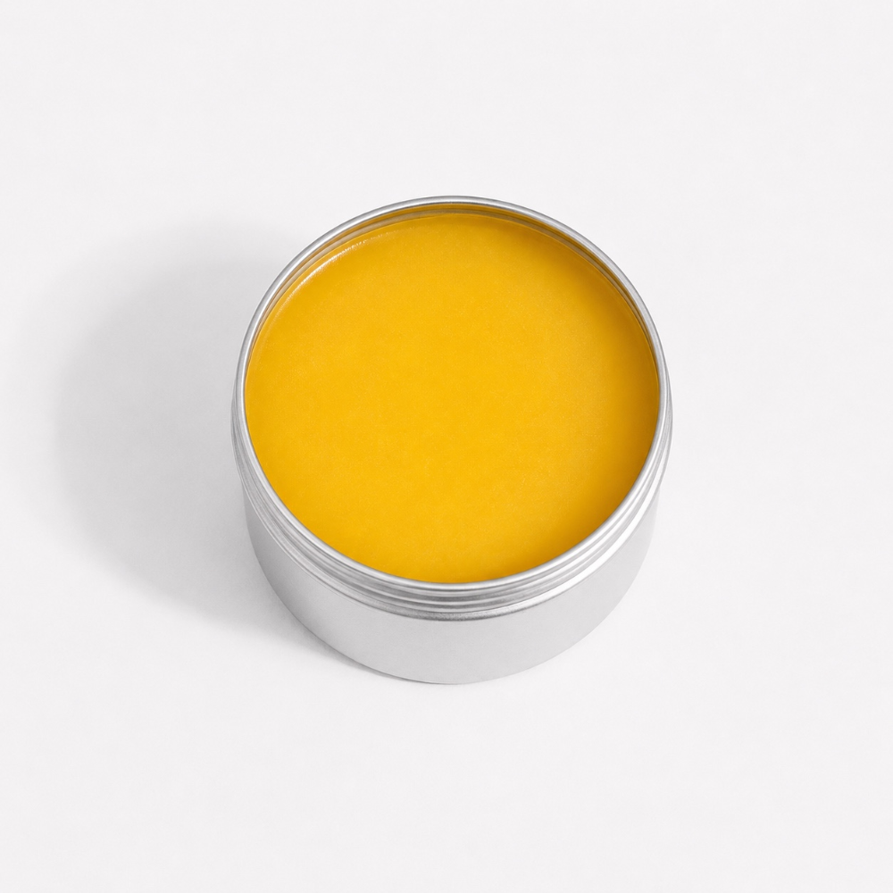 An open round silver metal tin filled with bright yellow balm or cream, photographed from above on a clean white background.