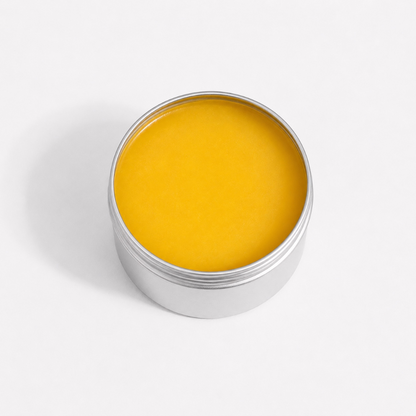 An open round silver metal tin filled with bright yellow balm or cream, photographed from above on a clean white background.
