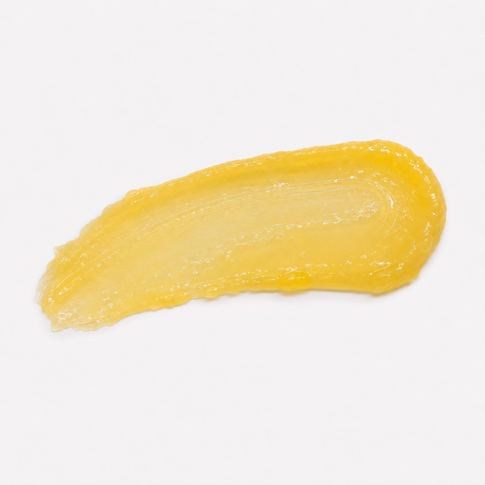 A textured smear of yellow skincare cream or gel on a plain white background.